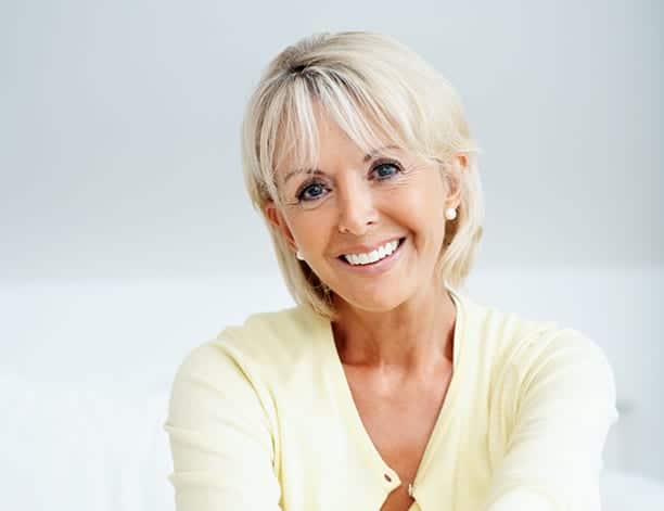 Relaxed mature woman sitting in couch against grey