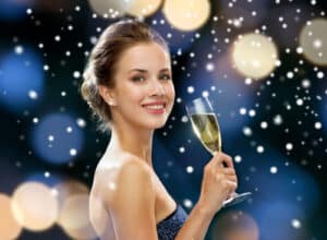 smiling woman in evening dress with glass of sparkling wine over night lights