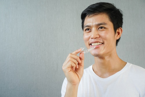 man smiling with hand holding dental aligner retainer 1