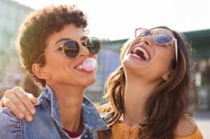laughing and chewing gum with friend embracing her.