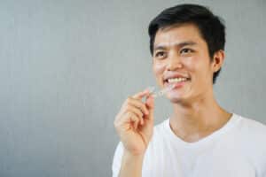 close up young asian man smiling with hand holding dental aligner retainer