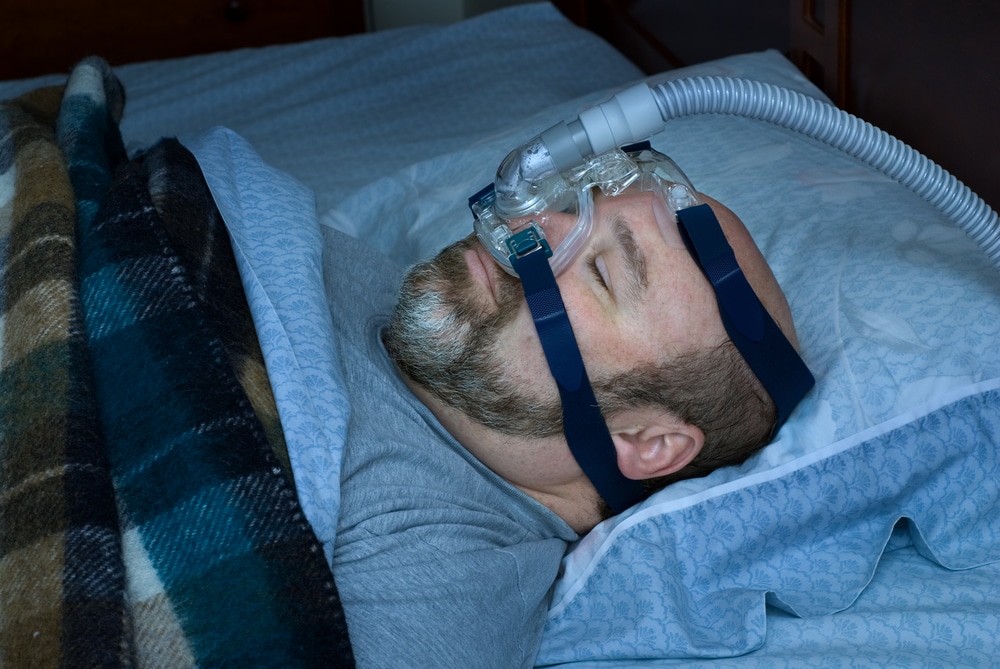Older man sleeping in his bed with a CPAP machine on to treat sleep apnea.