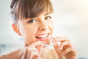 Young woman putting on her Invisalign clear aligners as part of her everyday routine for straighter teeth.