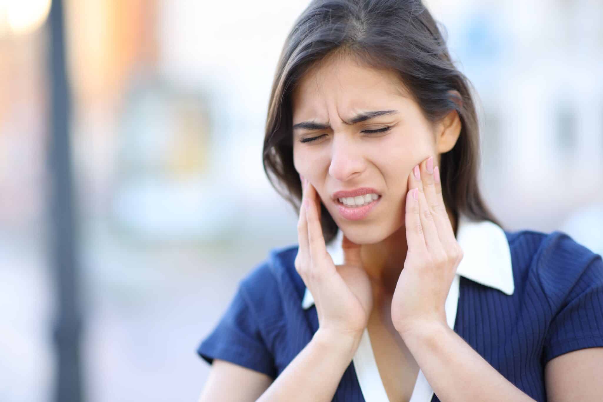 Young woman pushing on the sides of her jaw, in need of TMJ dental treatment.