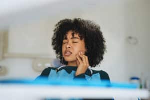 Woman in a dental chair touching her jaw near her ear, illustrating TMJ-related ear pain, pressure, or ringing.